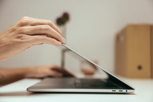 A close-up of a hand closing a laptop in a clean and minimal office setting, symbolizing the end of a work session.