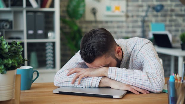 Tired office worker resting head on laptop at desk in a modern office.