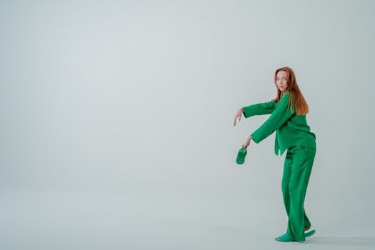 Woman in a green ensemble posing in a minimalist studio setting, showcasing modern fashion.